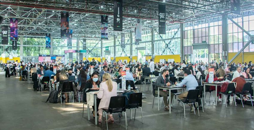 Muchas personas, sentadas en varias mesas ubicadas en un gran salón, charlando y haciendo negocios.