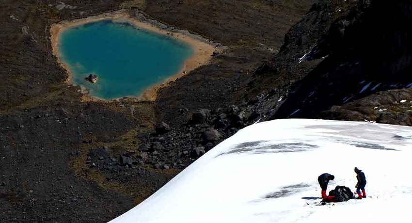 Dos personas de pie en zona de nieve y al fondo una laguna.