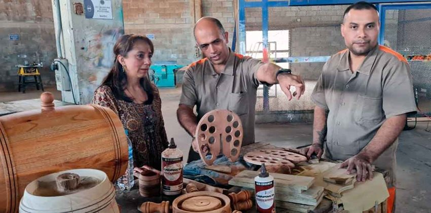 La viceministra Soraya Caro Vargas junto dos hombres hablando y observando artesanías en un taller.
