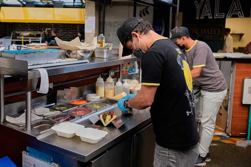 Cocineros de micronegocio gastronómico armando un perro caliente y hamburguesa.