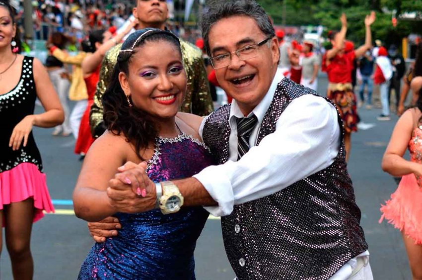 Hombre y mujer con trajes de salsa, bailando en medio de la calle durante la feria.