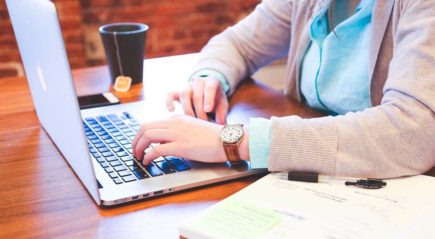 Manos de mujer escribiendo en un computador portátil.