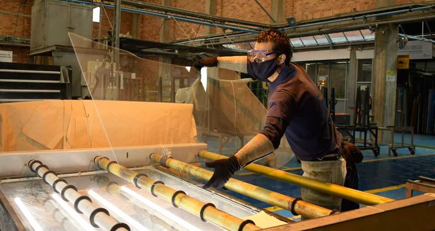 Hombre manipulando un vidrio sobre una máquina, en una fábrica.