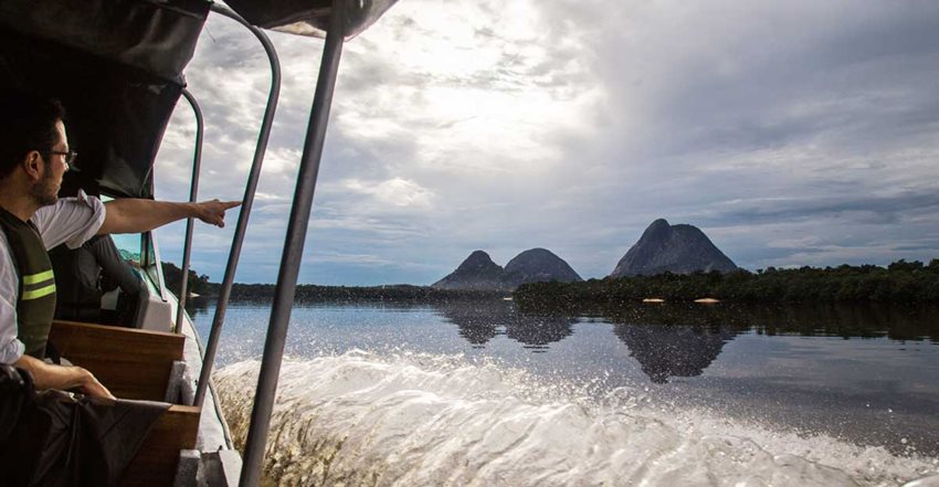 Hombre en lancha señalando las montañas en medio de un río.