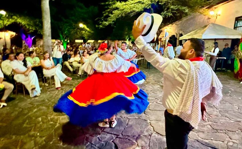 Descripción de la imagen: Personas bailando con trajes típicos de Colombia, en medio de un parque, en la noche.