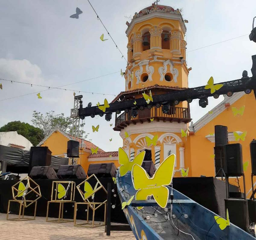Tarima, en medio del parque, con mariposas amarillas de luces y detrás la torre de la iglesia de Mompox.