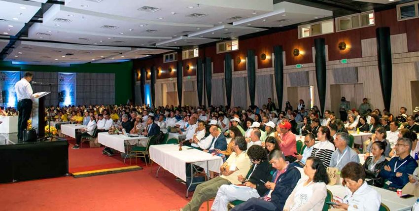 Personas sentadas en sillas en auditorio, prestando atención al ponente en el escenario.