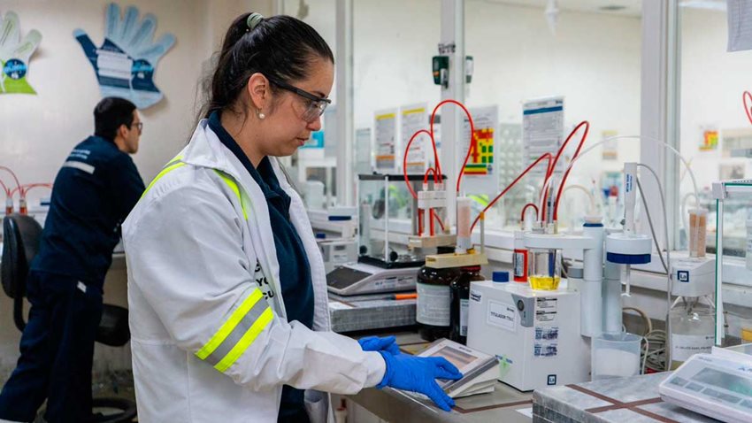 Mujer con traje de laboratorio y de seguridad, manipulando objetos de laboratorio.