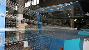 Operario al lado de una máquina que está fabricando hilos. - Gobierno impone arancel cero a 37 subpartidas correspondientes a insumos y materias primas usadas para hacer confecciones y zapatos