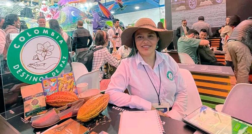 Mujer con sombrero y camisa blanca posando para la foto junto al sello Colombia, destinos de paz.