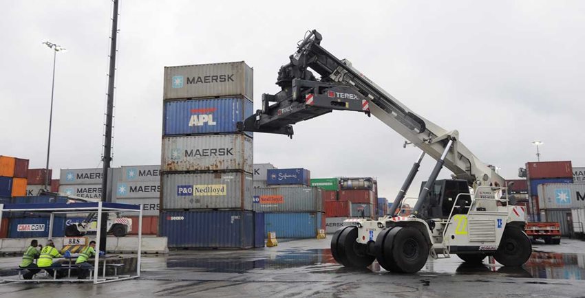 Carro maquinaria blanco, como especie de grúa, cargando contenedores de colores.