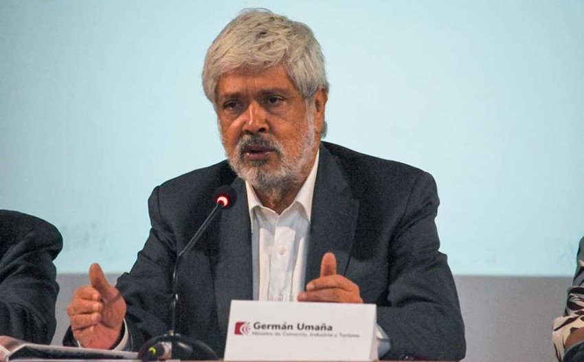 Ministro Germán Umaña hablando al público por medio de un micrófono y sentado en una mesa.