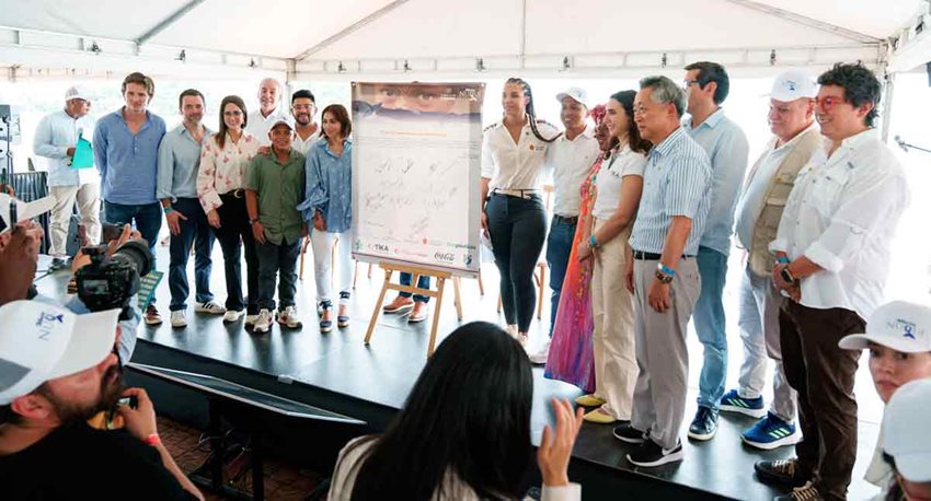 Descripción de la imagen: Hombres y mujeres posando para la foto en el escenario, al lado de cartelera.