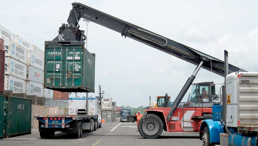 Máquina descargando contenedor verde sobre tráiler de un camión.