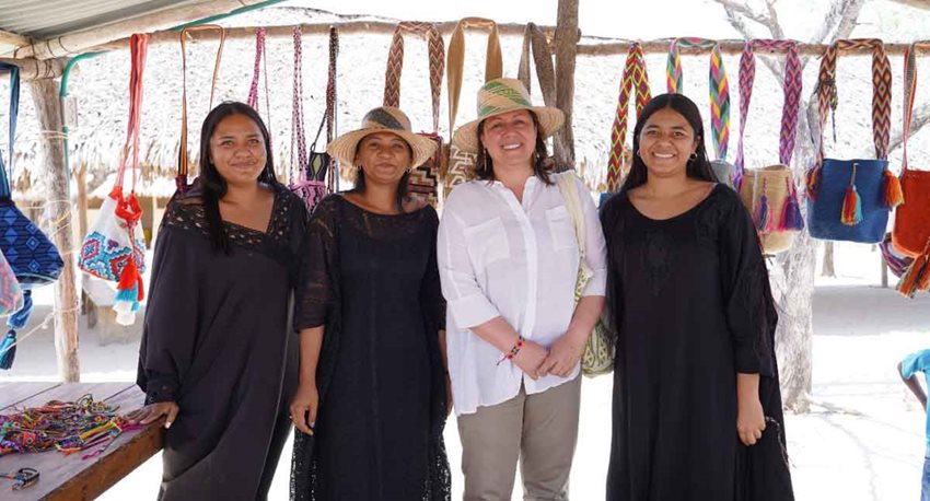 Ministra María Ximena Lombana con artesanas de la comunidad wayúu y de fondo mochilas tejidas por ellas.