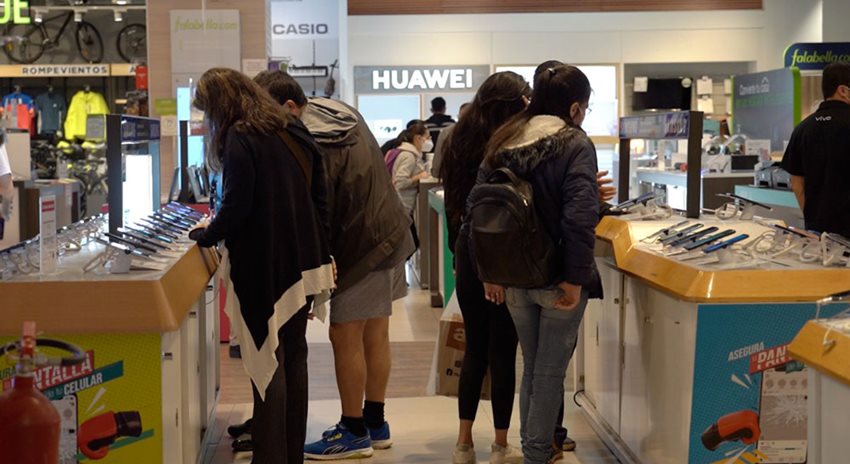 Personas en sección de tecnología, de almacén de cadena, comprando productos durante el día sin IVA.