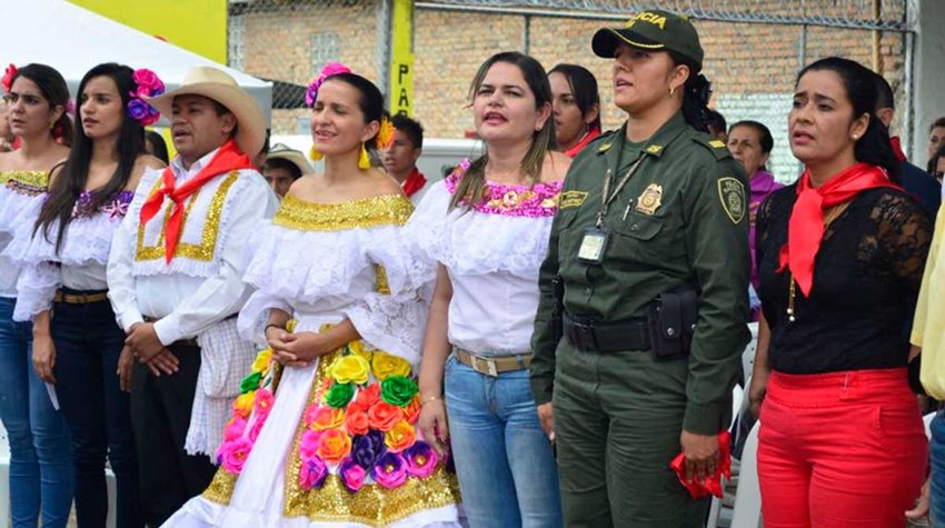 Diferentes mujeres de pie, con trajes típicos de Colombia y uniformes de policías.