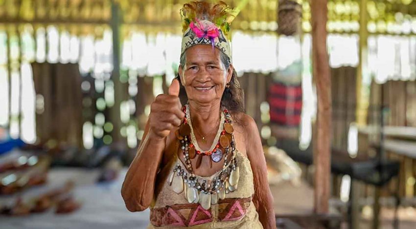 Mujer indígena, de la tercera edad, con traje típico y sonriendo y saludando.