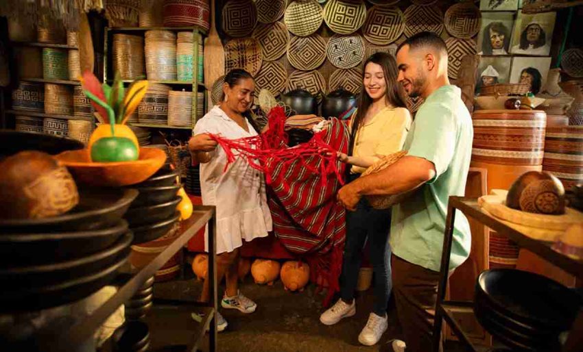 Dos mujeres y un hombre mirando una hamaca roja, en medio de un cuarto lleno de artesanías.