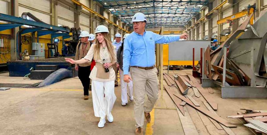 Ministra Diana Morales, con elementos de seguridad caminando, junto a un señor, por planta de industria naval.