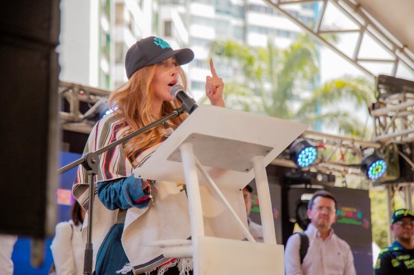 Ministra Diana Morales hablando por micrófono, en atril, desde el escenario.