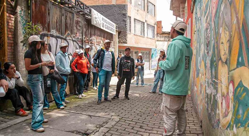 Personas caminando, de día, por calles de un barrio de Bogotá, mientras les dan explicaciones.