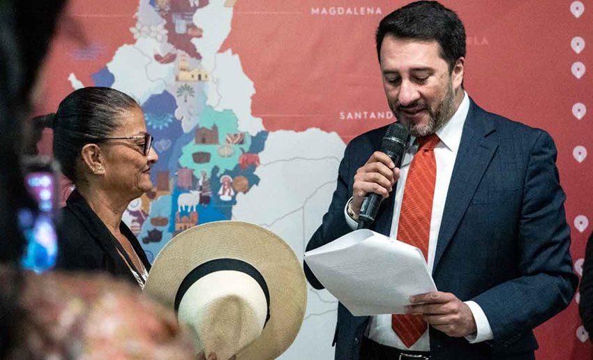 Descripción de la imagen: Mujer con sombrero en la mano, junto al viceministro de Turismo, Arturo Bravo, mientras habla por micrófono.