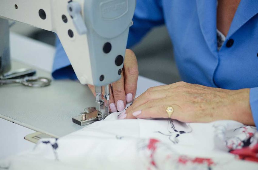 Fotografía de manos de mujer en una máquina de coser arreglando una prenda.