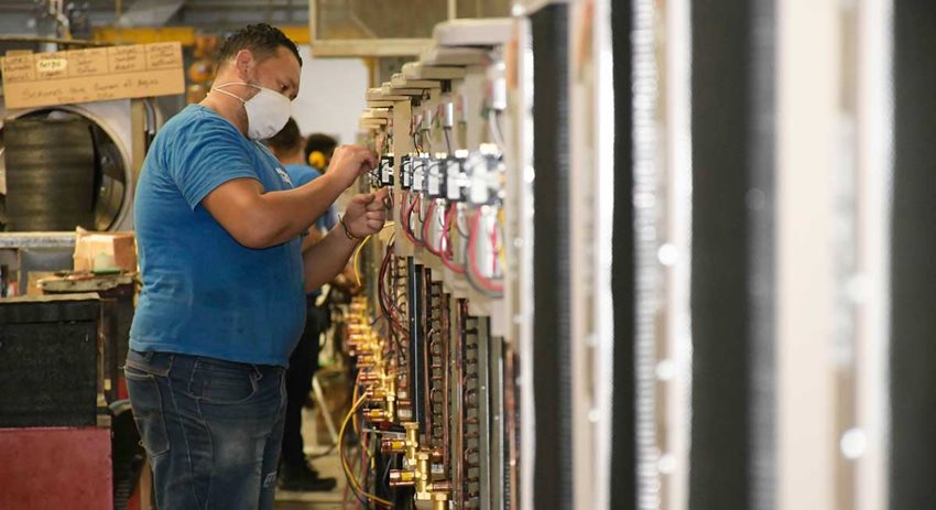Hombre, con tapabocas y de pie, frente a una máquina trabajando.