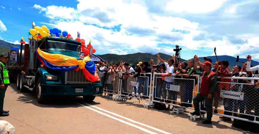 Personas observando camión decorado con bombas y bandera de Colombia, que va pasando por vía del puente.