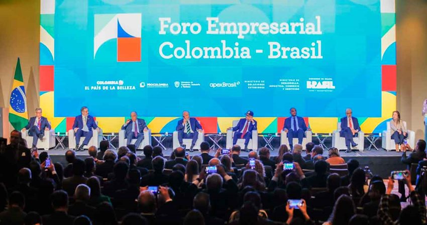 Descripción: 7 hombres y 1 mujer, funcionarios de Brasil y Colombia, sentados en sillas en el escenario frente al público.